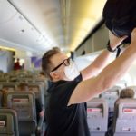 Un pasajero con mascarilla, colocando su maleta en el compartimento de un avión.