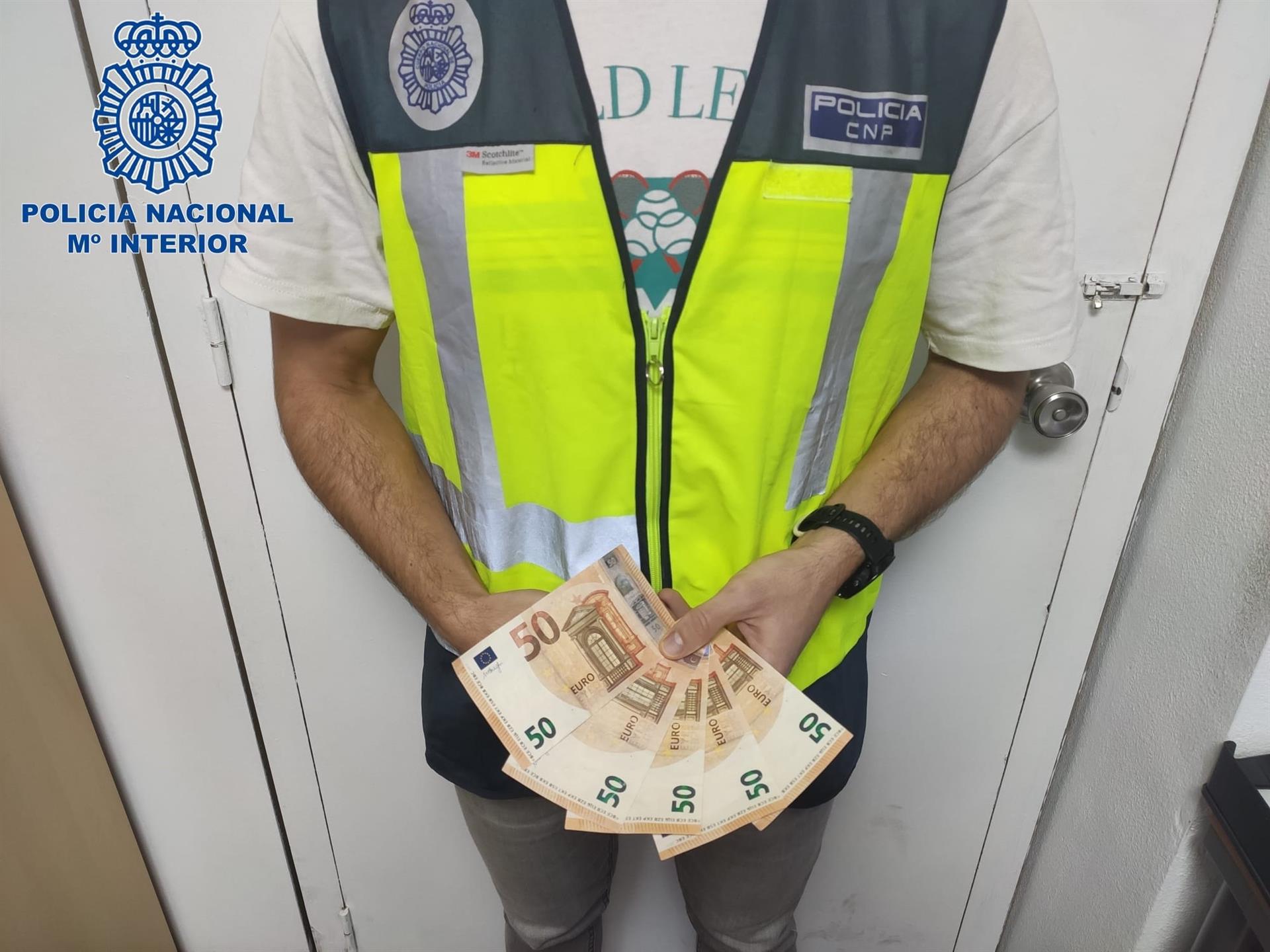 Un agente de la Policía muestra los billetes falsos con los que el joven detenido compró artículos en puestos ambulantes navideños en Palma - POLICÍA NACIONAL