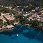 Vista superior del complejo turístico en un acantilado rocoso en Canyamel, Cala Serch en Mallorca, con un solitario yate en un mar turquesa.
