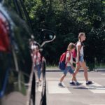 Niños cruzan la calle rumbo al colegio frente a un coche parado.