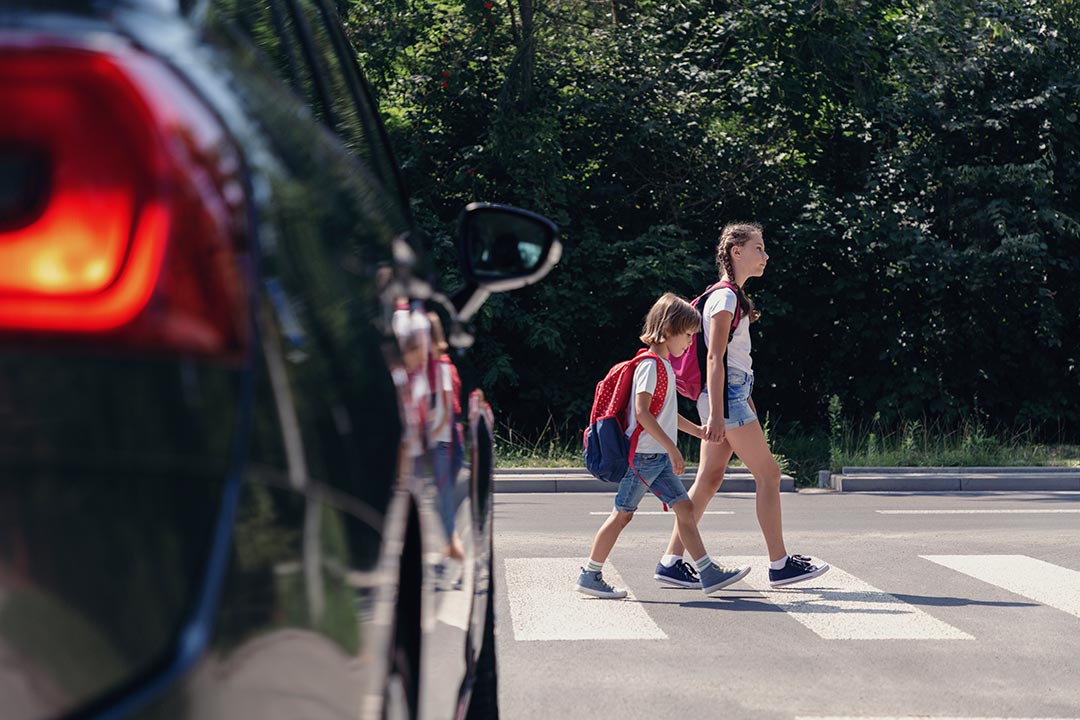 Niños cruzan la calle rumbo al colegio frente a un coche parado.