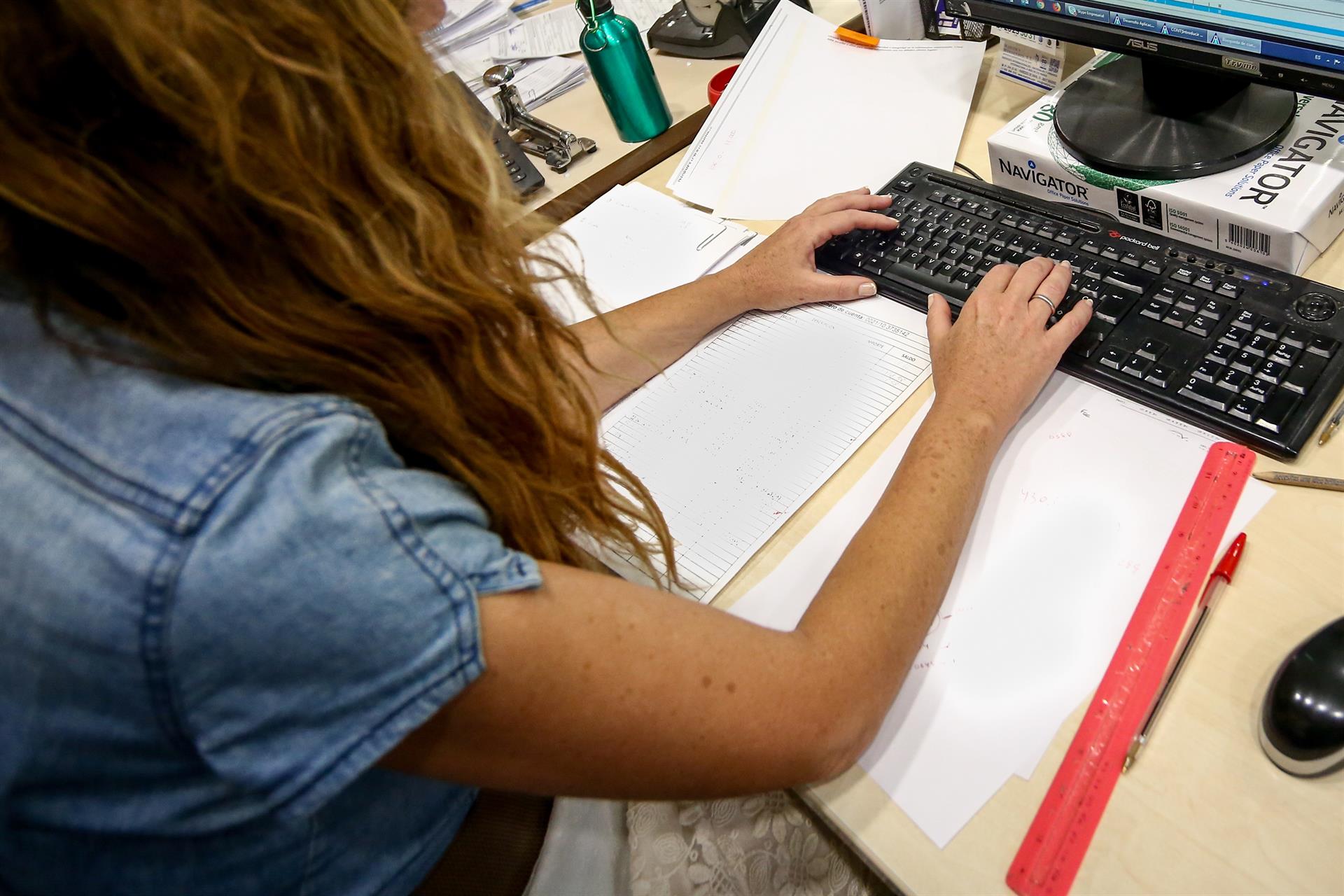 Una mujer escribe en el teclado de su ordenador, con papeles alrededor mientras trabaja en la oficina. - RICARDO RUBIO / EUROPA PRESS - Archivo